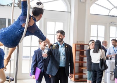 Aerial performer in a blue costume pours champagne for a smiling man in a suit at an indoor event with guests socializing in the background.