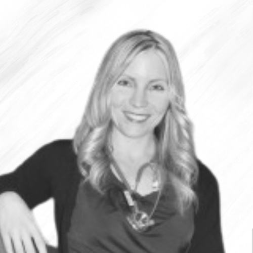 A woman with long, wavy blonde hair is smiling. She is wearing a dark top, a light necklace, and a dark cardigan. The background is plain and light-colored.