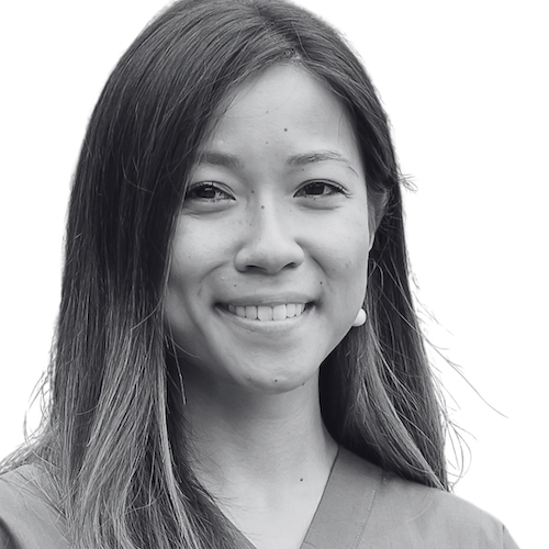 A woman with straight, shoulder-length hair is smiling at the camera. She is wearing a V-neck top and appears against a plain white background. The image is in black and white.