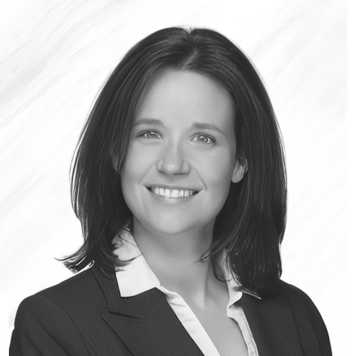 A woman with straight dark hair, wearing a suit jacket over a white collared shirt, smiles at the camera in a black-and-white portrait with a plain background.